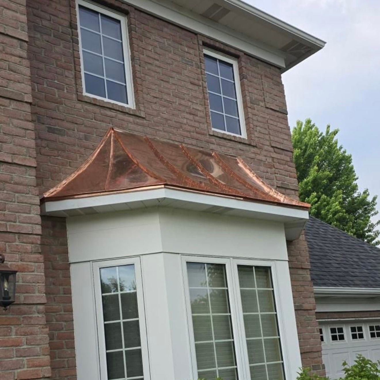 A brick house facade features a white bay window topped with a copper-accented roof.