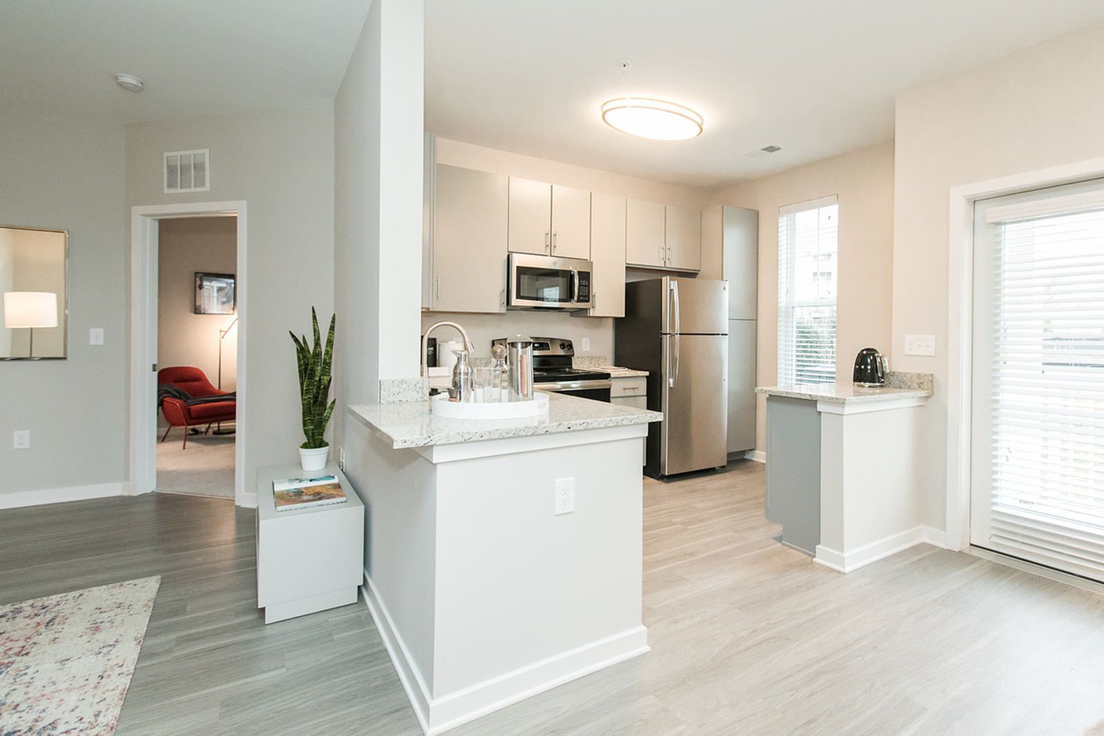Bright modern kitchen and living area with white cabinets, stainless appliances, and light wood flooring at The Villas at Mill Run Apartments in Owings Mills, MD