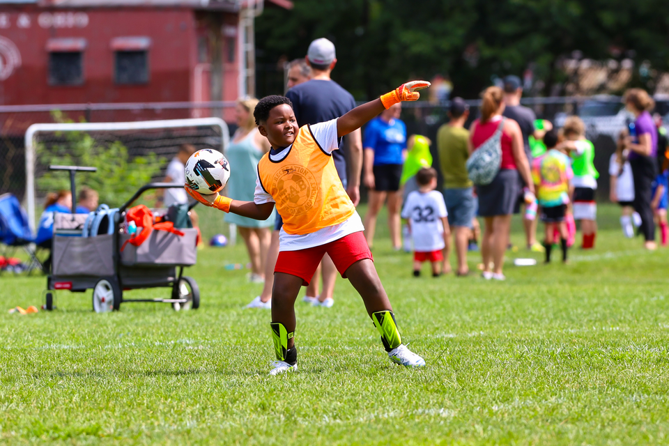Soccer player in orange jersey kicks a ball on a grassy field during practice