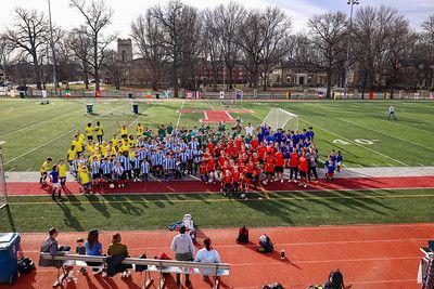 Crowd gathered on a sports field, with groups in yellow, red, and blue forming a colorful lineup.