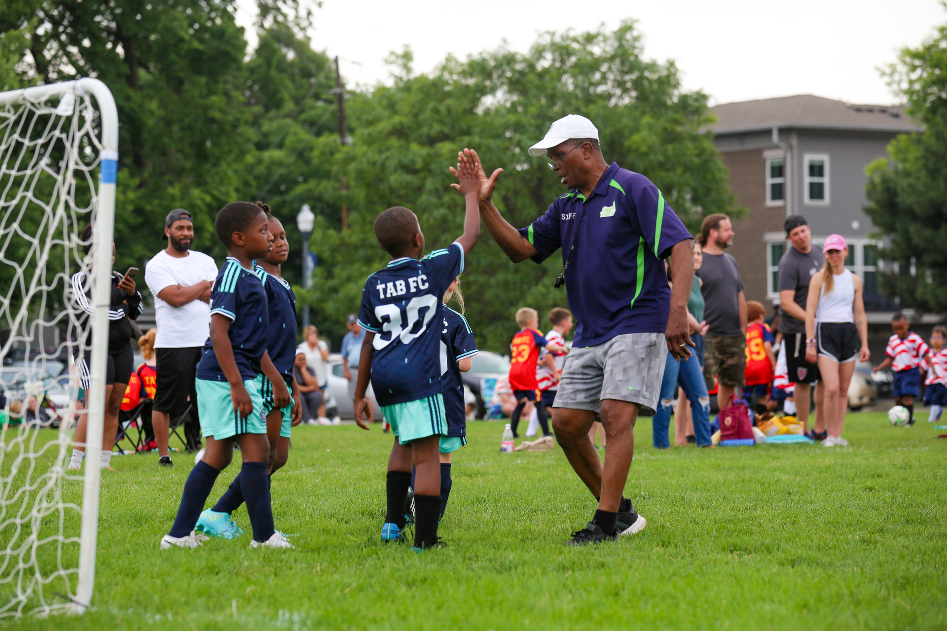 Youth soccer coach gives a high-five to a player beside a goal on a grassy field