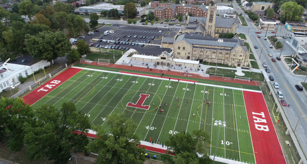 Aerial view of a football stadium with a green field and red end zones, surrounded by campus buildings and roads
