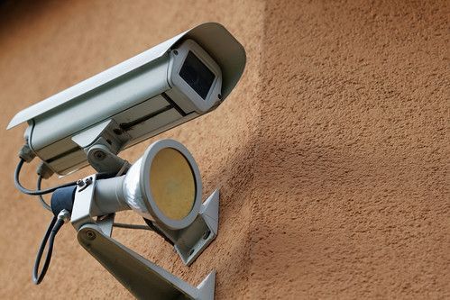 Outdoor security camera with floodlight mounted on a textured wall.