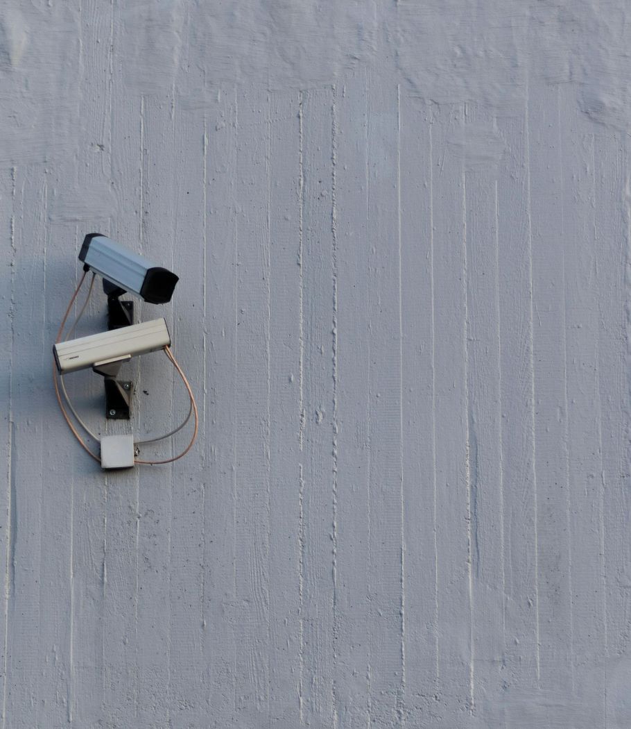 Two white surveillance cameras mounted on a weathered concrete wall.
