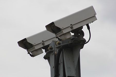 Two outdoor security cameras mounted on a pole against a cloudy sky.