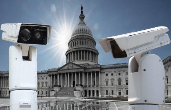 Two white outdoor security cameras mounted on a pole against a blue sky.