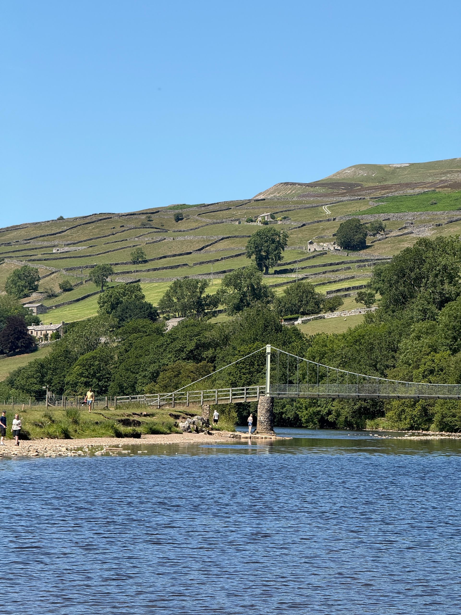 Lake with blue water, grassy hillside, and a small dock beneath a clear sky.