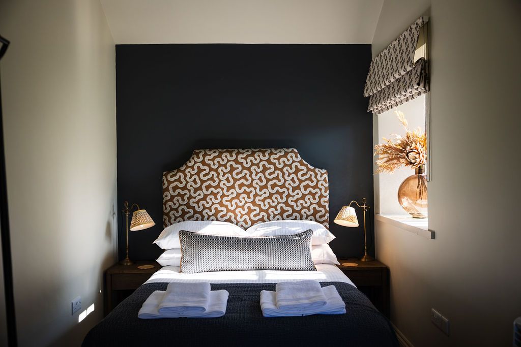 Modern bedroom with dark accent wall, patterned headboard, and neatly made bed by a window