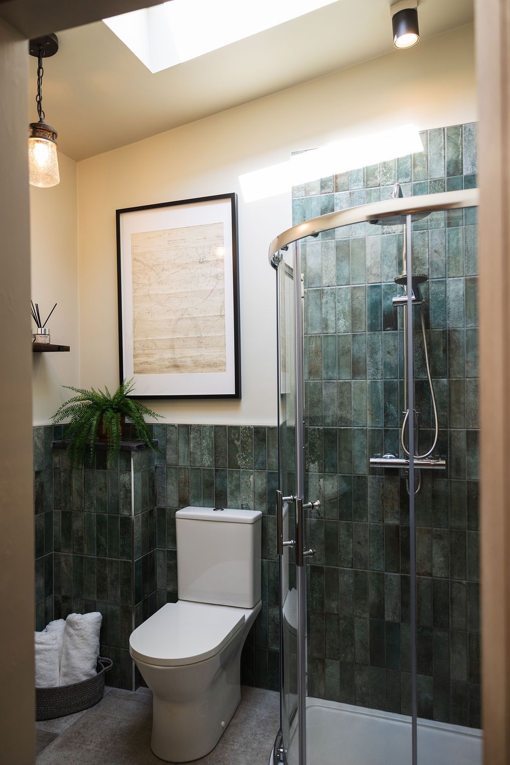 Modern bathroom with a toilet, glass shower, green tile walls, and framed wall art.