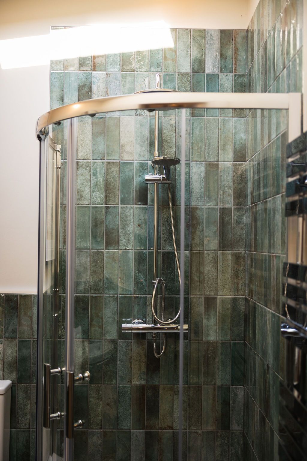Glass shower stall with green tiled walls and chrome fixtures