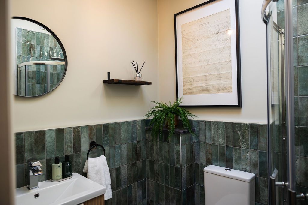 Modern bathroom with green tile, round mirror, sink, toilet, and shower.