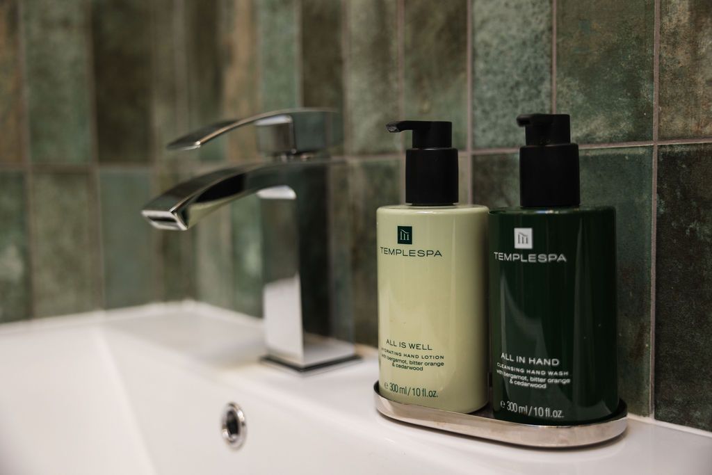 Bathroom sink with chrome faucet and two pump soap bottles on a tray against green tiled wall