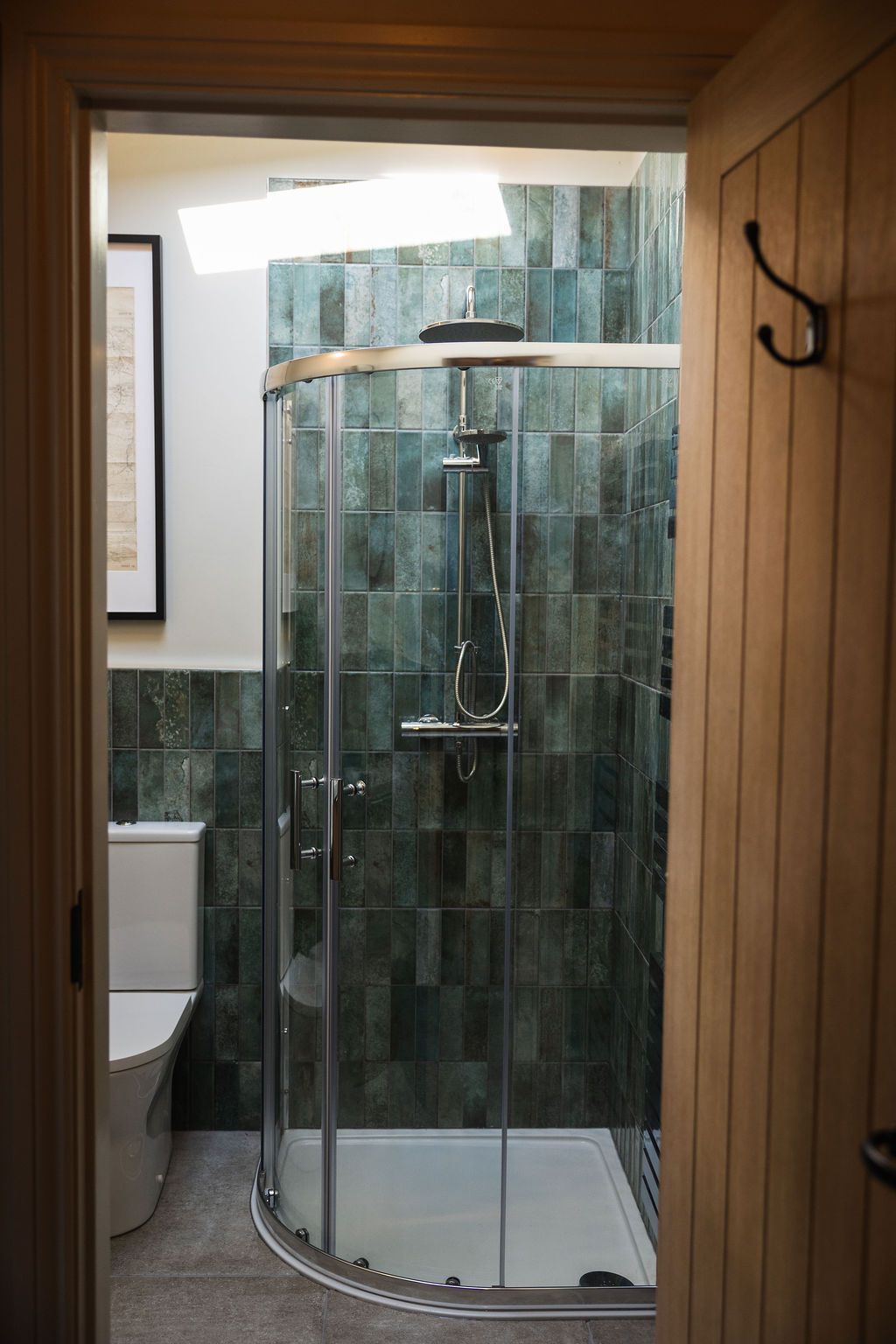Bathroom with a glass shower stall and tiled walls, viewed through a doorway.
