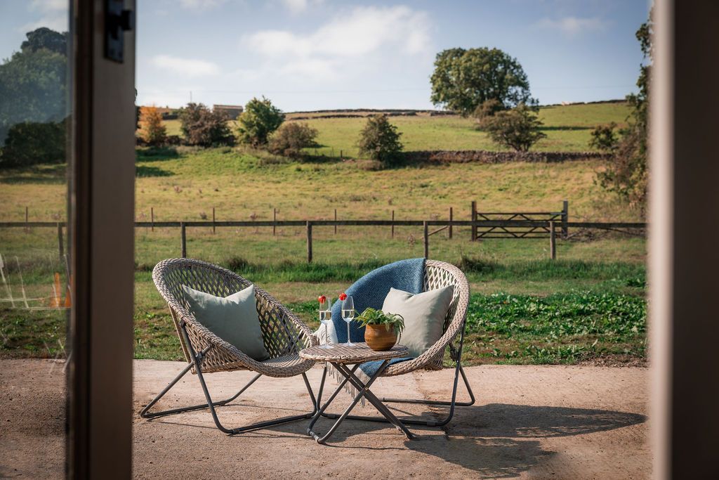 Two wicker chairs on a patio overlooking a sunny rural field and fence