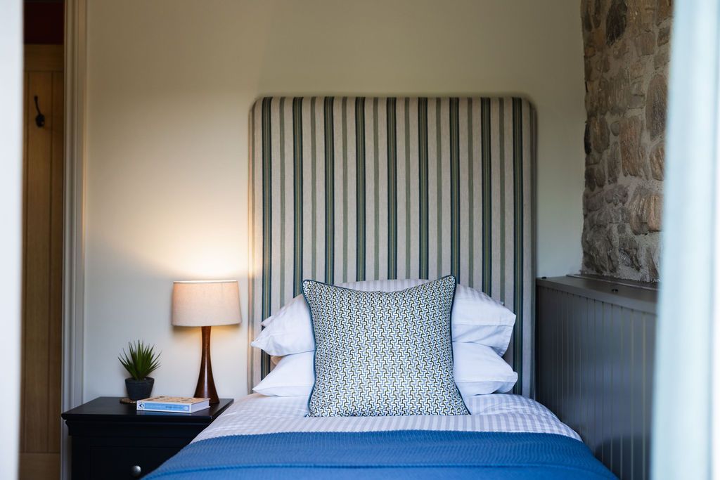 Cozy bedroom with a striped headboard, blue bedding, bedside lamp, and small plant on a nightstand