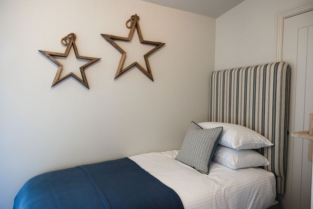 Small bedroom with a neatly made bed, blue blanket, striped pillow, and star wall decorations.