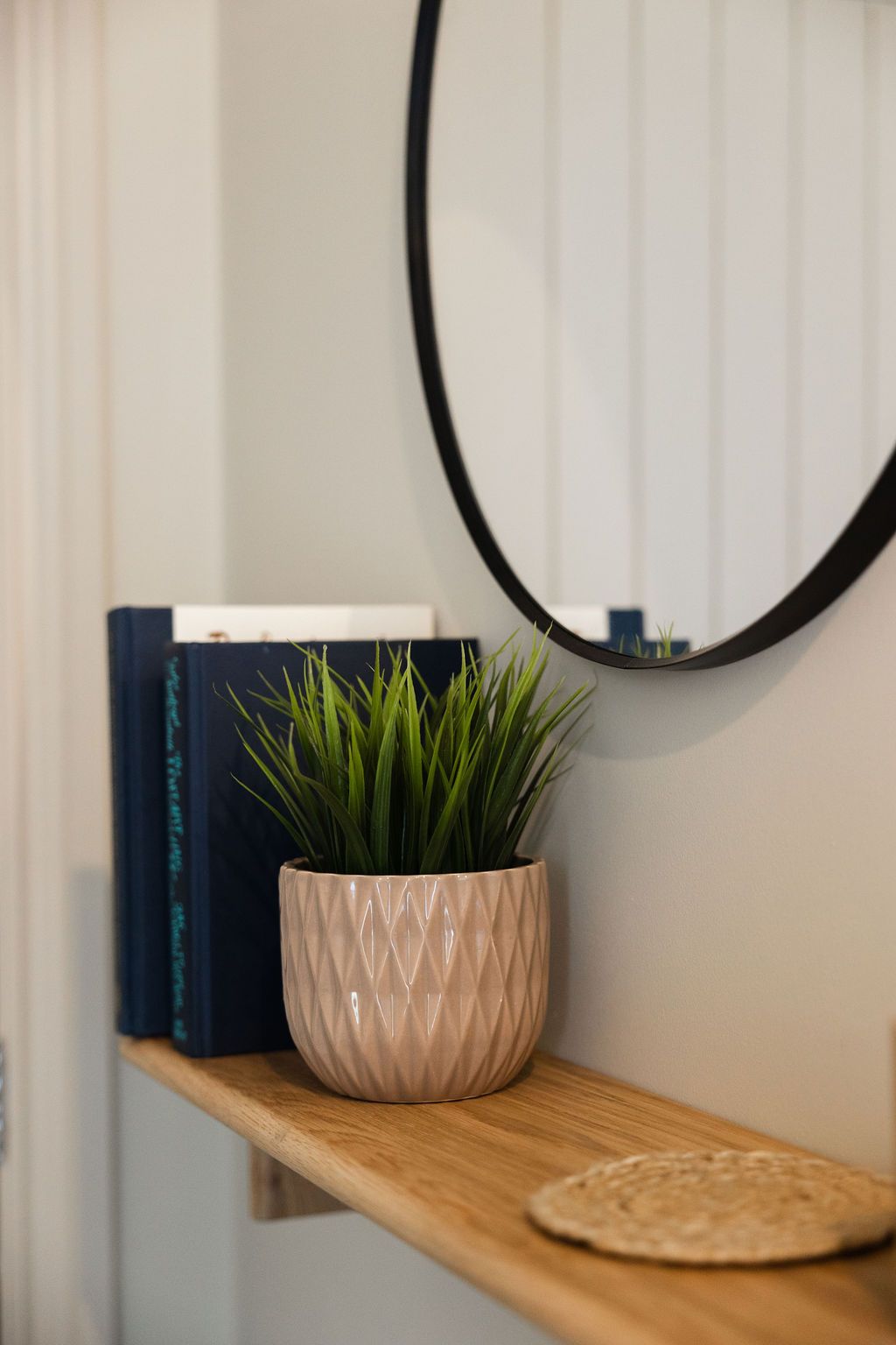 Small shelf with books, a potted plant, and a round wall mirror in a bright room.