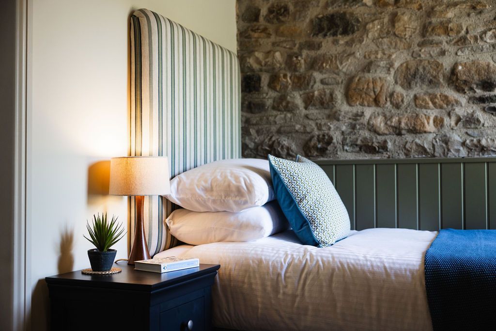 Cozy bedroom with striped headboard, white bedding, bedside lamp, and stone accent wall