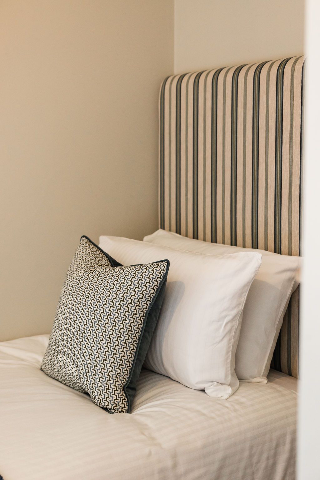 Striped upholstered headboard with white bedding and a black-and-white accent pillow on a bed