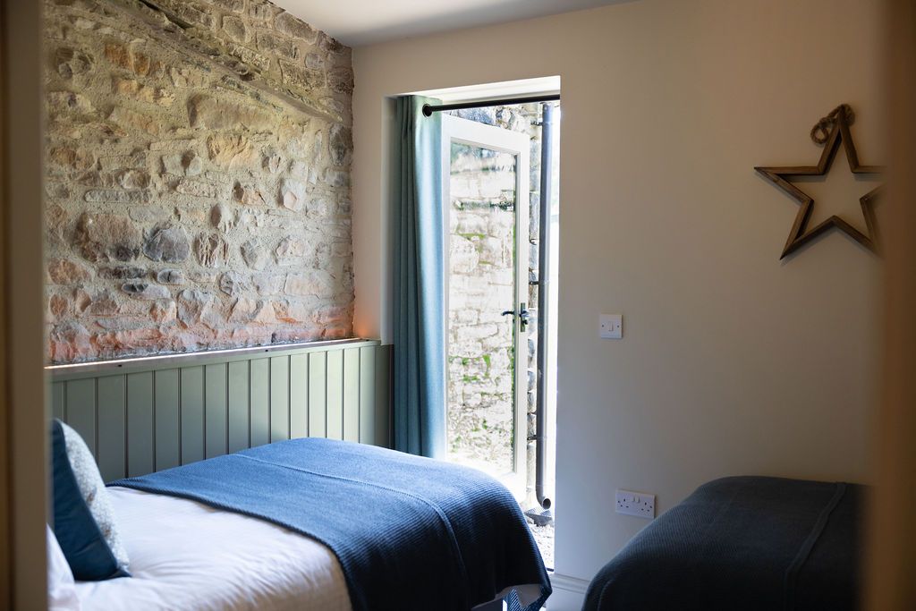 Small bedroom with two beds, stone accent wall, and open door to a bright balcony.