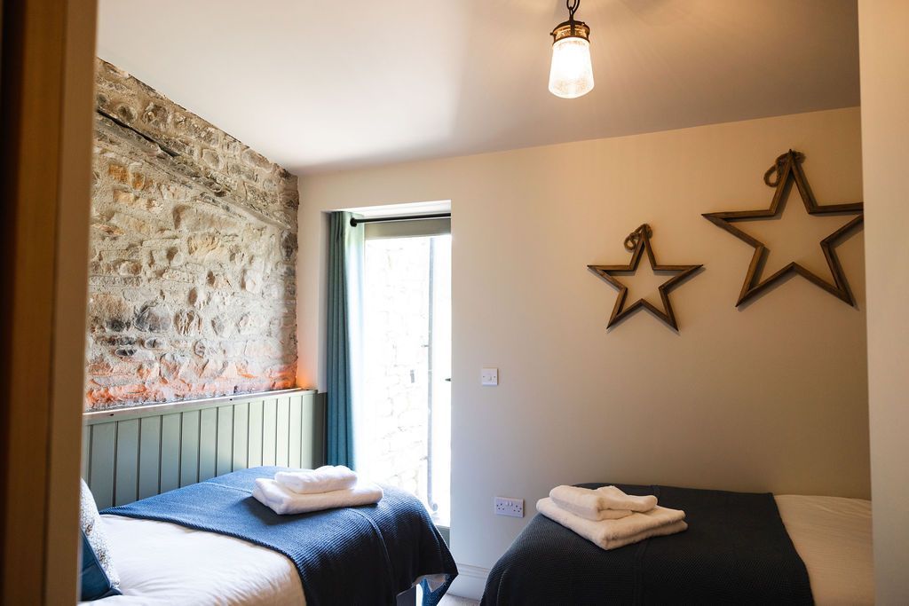 Small bedroom with two single beds, star wall decor, patterned wallpaper, and a bright open doorway