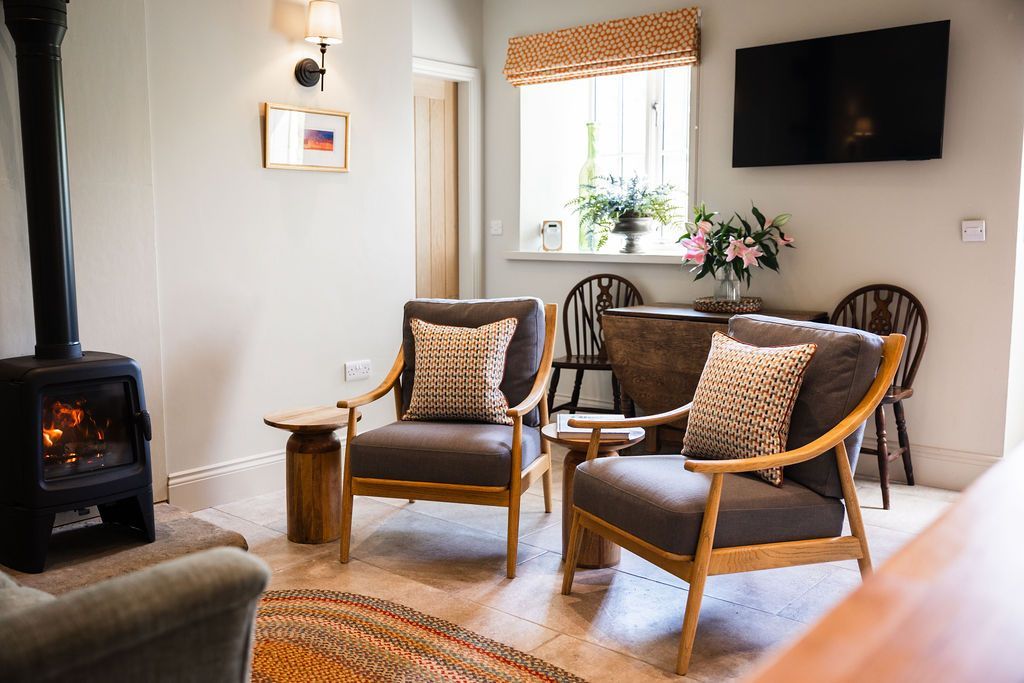 Cozy living room with two wicker chairs, wood stove, wall TV, and window with flowers