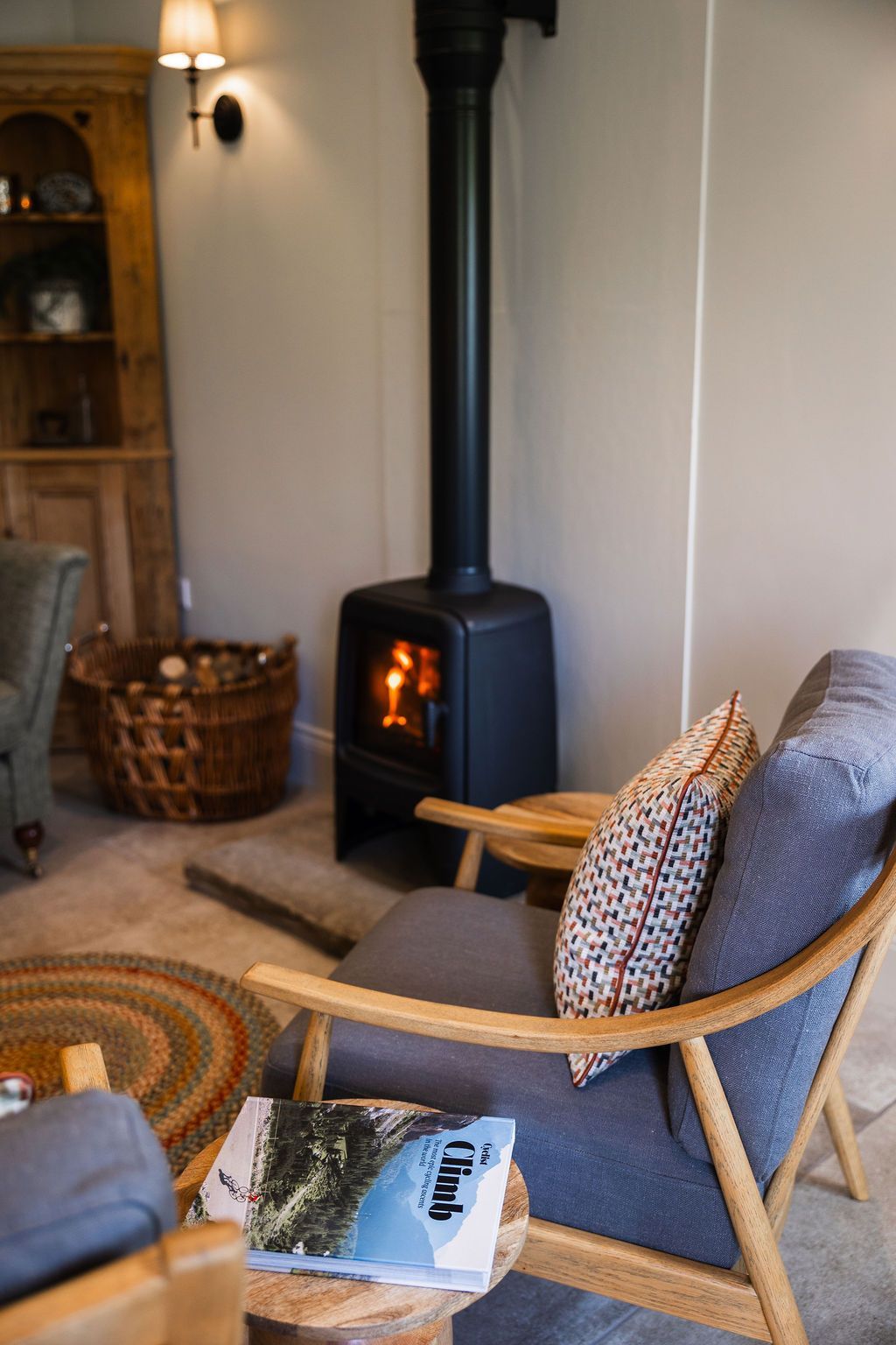 Cozy living room with black wood stove, gray chair, and woven basket near a wall lamp