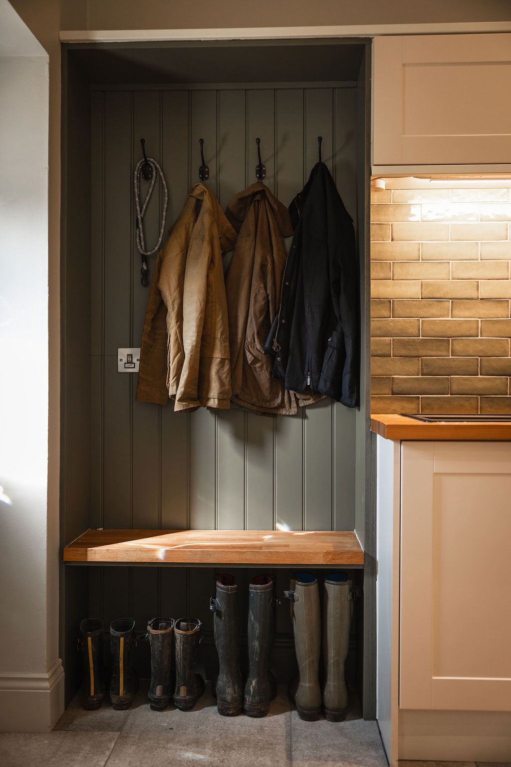Built-in entryway nook with coats on hooks, a bench, and boots stored below