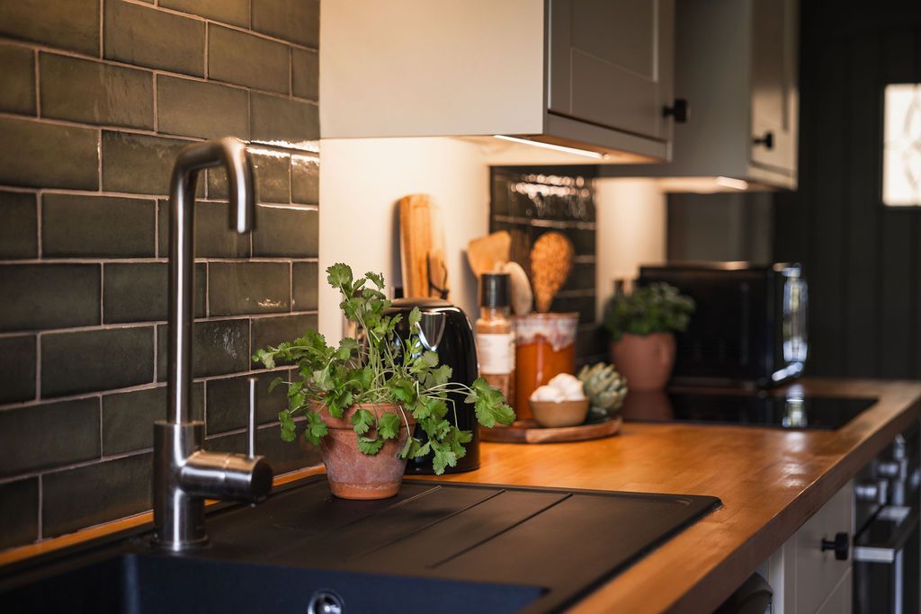 Modern kitchen countertop with black sink, wooden counters, plants, and tiled backsplash
