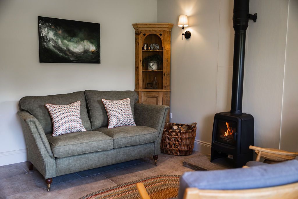 Cozy living room with gray loveseat, wood-burning stove, wall art, and wood cabinet