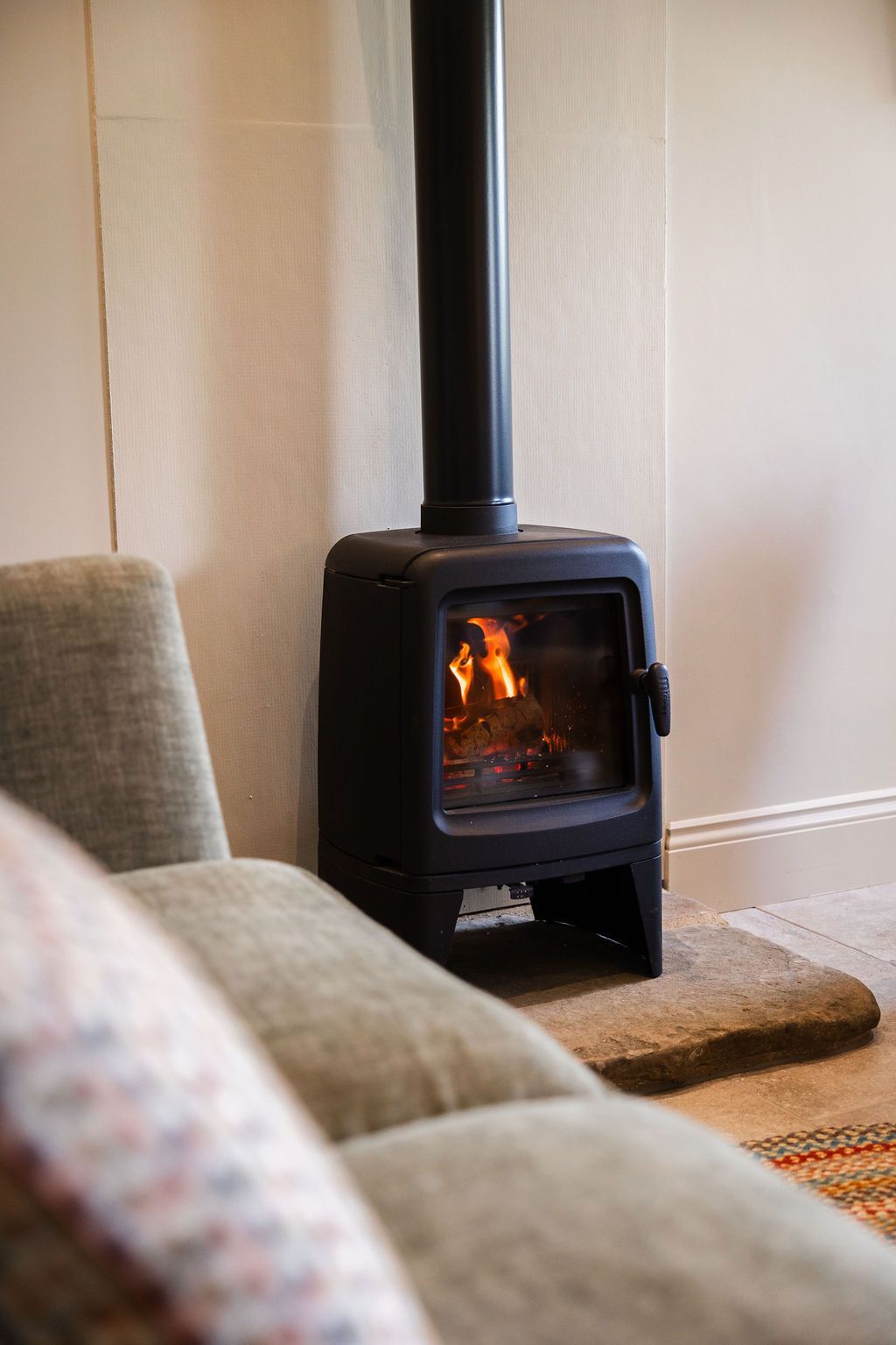 Black wood stove with a fire burning in a cozy living room beside a gray sofa