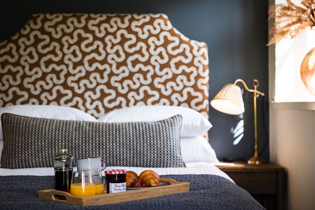 Cozy bed with patterned headboard, gray bedding, bedside lamp, and breakfast tray in a hotel room