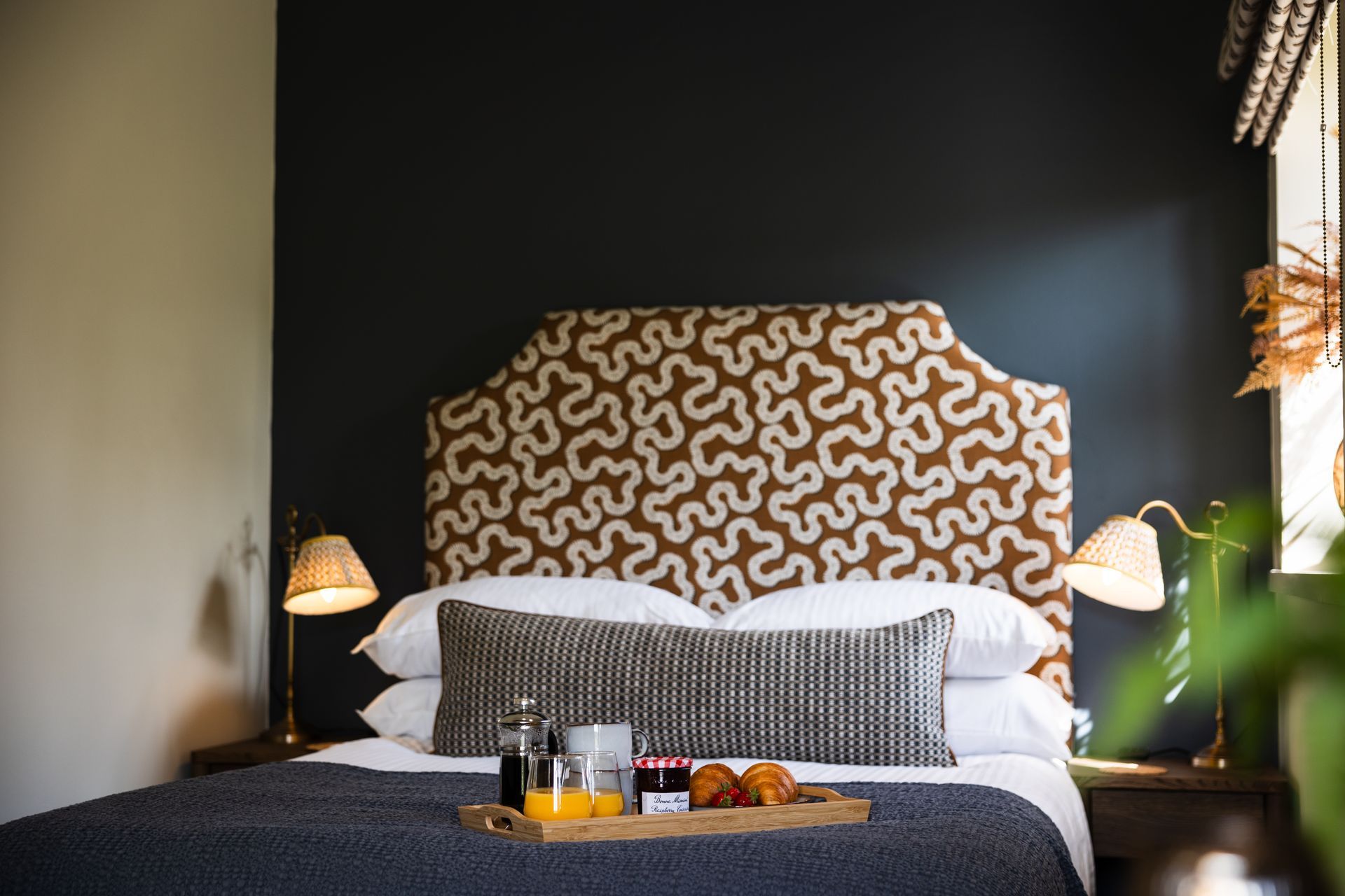 Modern bedroom with patterned headboard, bedside lamps, and breakfast tray on the bed