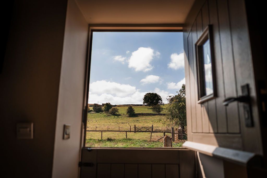 View through an open doorway to a sunny green field and blue sky with clouds