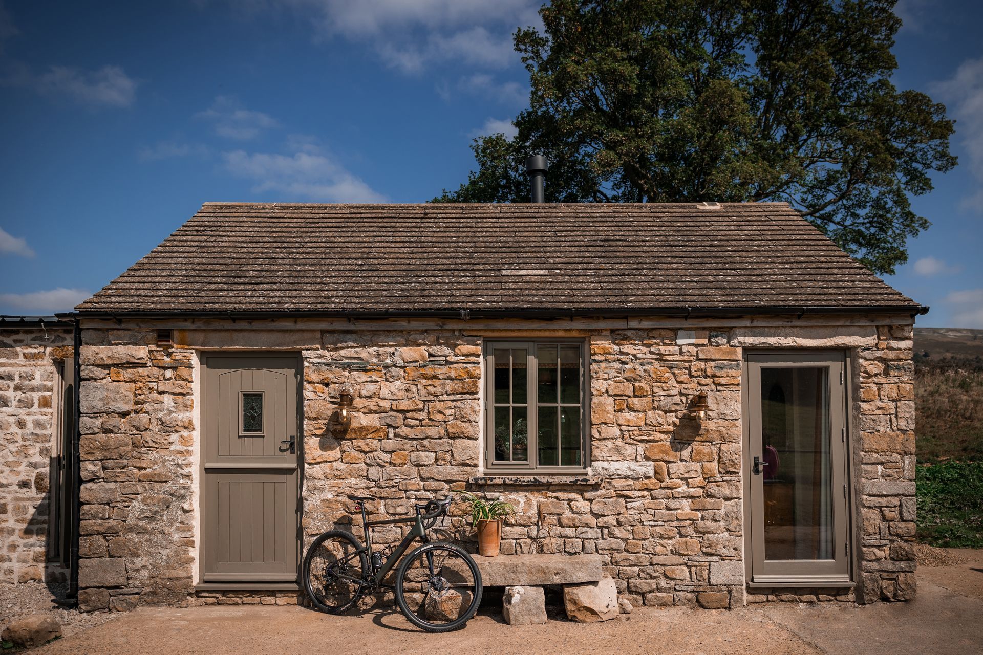 Small stone cottage with a bicycle by the door under a blue sky