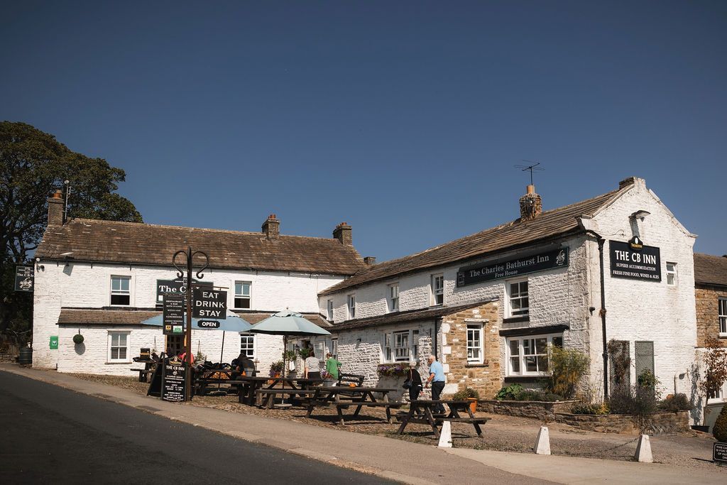 White thatched pub with outdoor tables on a sunny street corner under a clear blue sky.