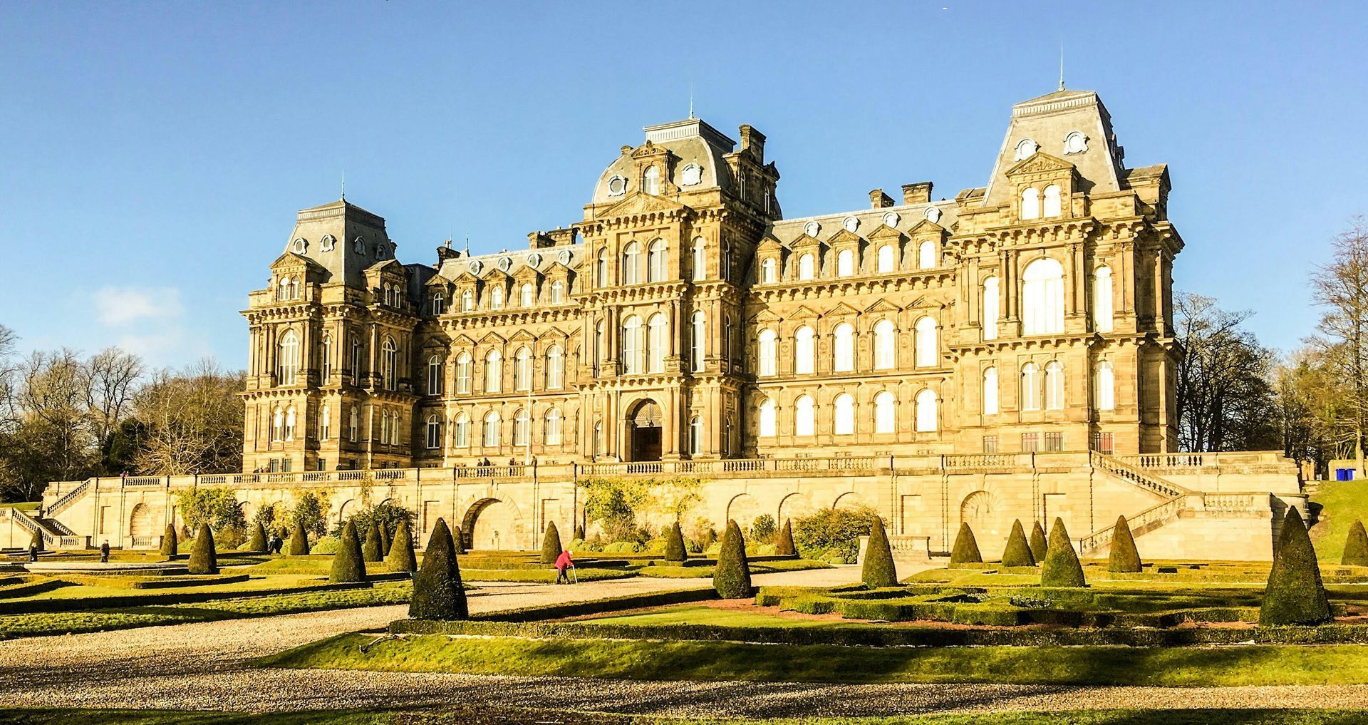 Grand historic palace with ornate stone фасade and gardens under a clear blue sky