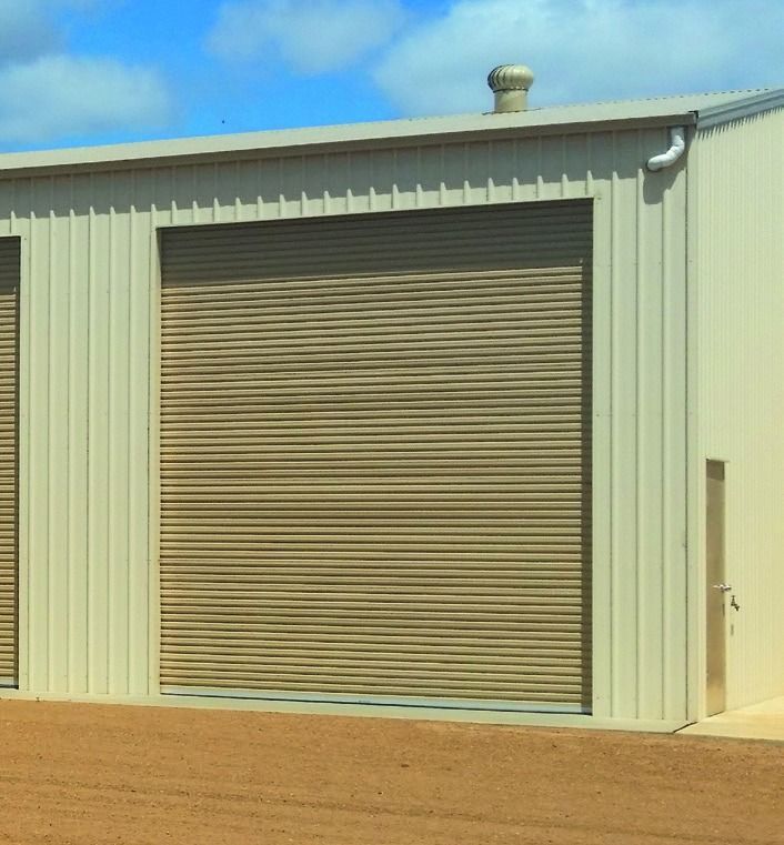 Closed metal garage door behind a green hedge and paved walkway