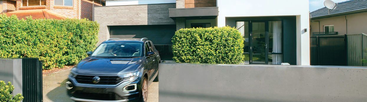 Closed metal garage door behind a green hedge and paved walkway
