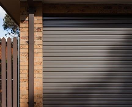 Closed gray metal garage door beside a brick wall and white fence