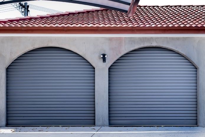 Closed metal garage door behind a green hedge and paved walkway