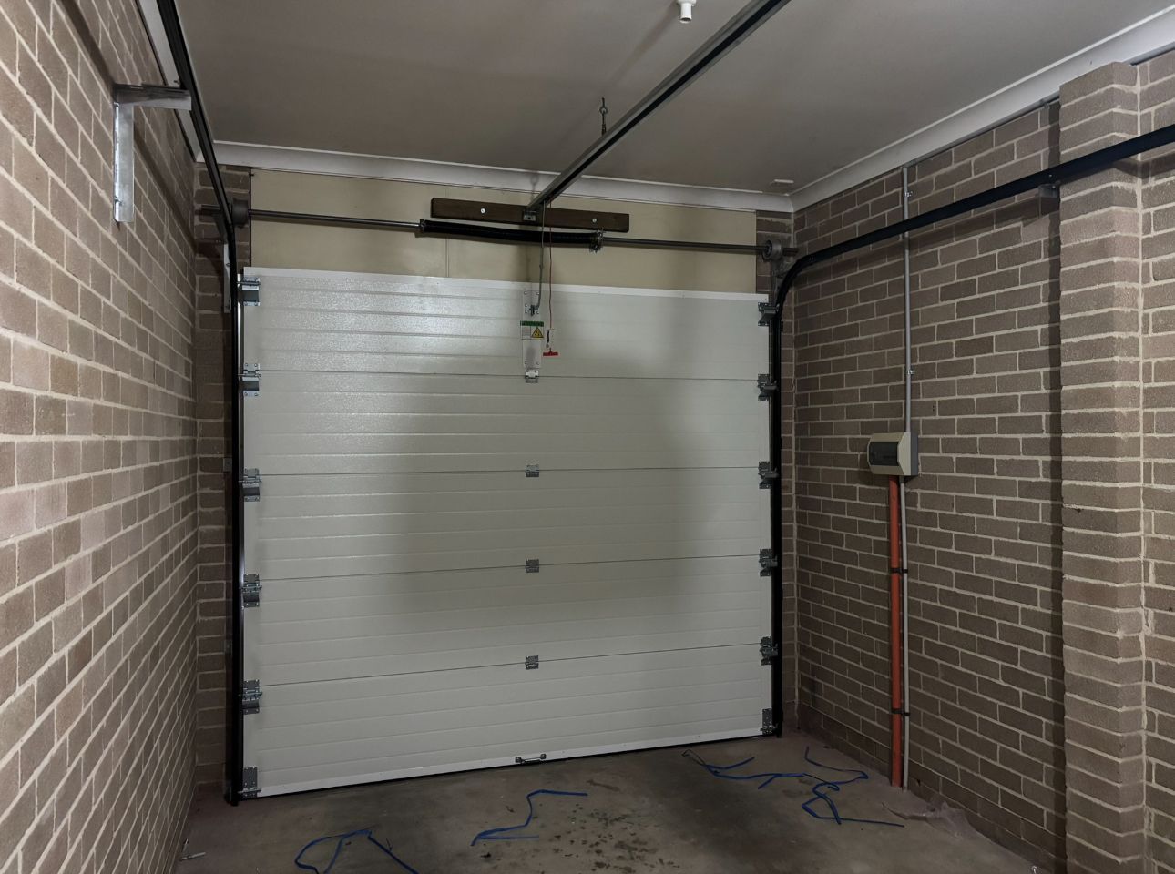 Garage interior with a closed white sectional door and brick walls on both sides