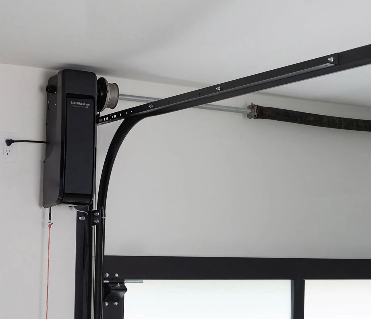 Black garage door opener mounted on ceiling near a window.