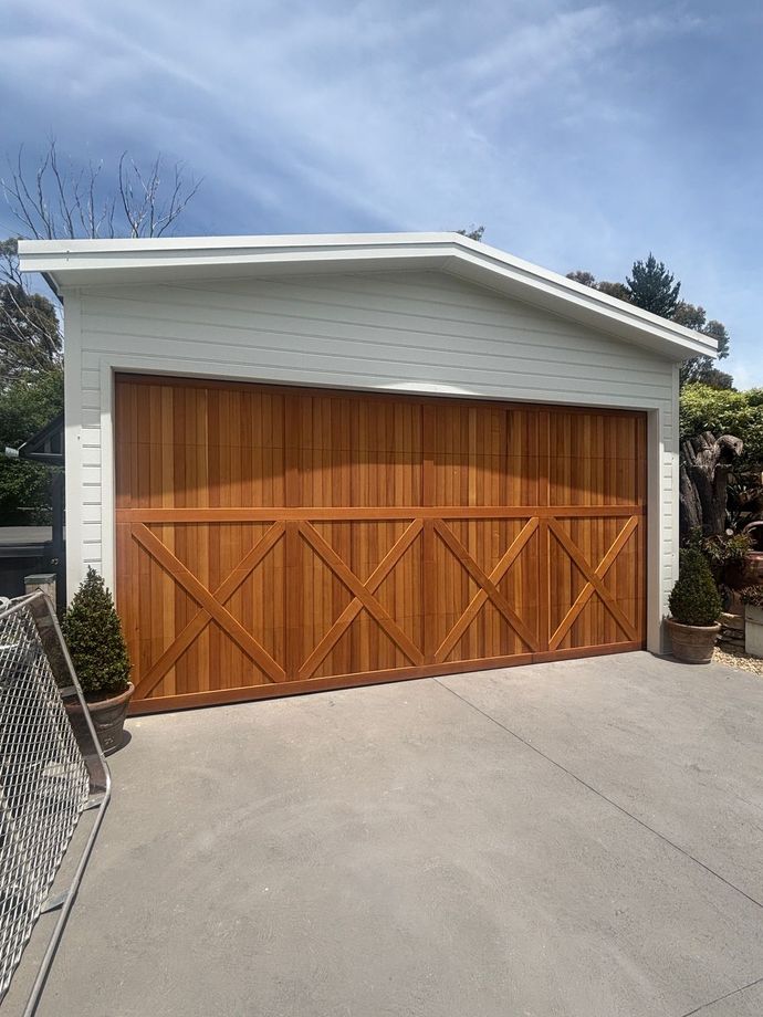 White garage with wooden double doors and a concrete driveway under a blue sky