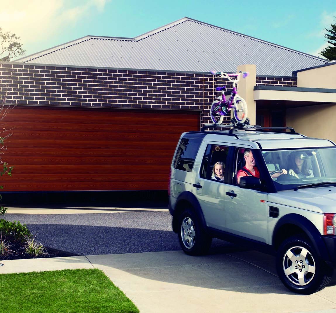 White SUV in a driveway with a bicycle mounted on the roof, in front of a suburban garage.