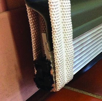 Close-up of a damaged window blind with torn woven trim and a black broken section near the bottom