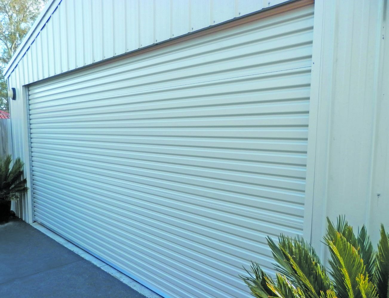 Closed metal garage door behind a green hedge and paved walkway