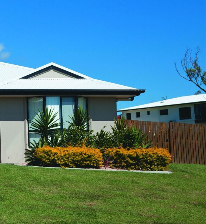 Modern house with white roof, green lawn, and orange shrubs under a bright blue sky