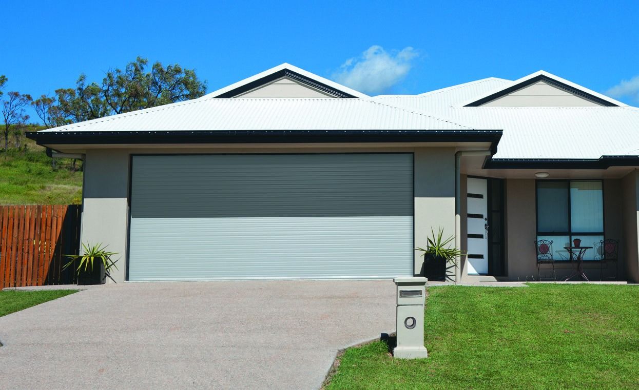 Closed metal garage door behind a green hedge and paved walkway