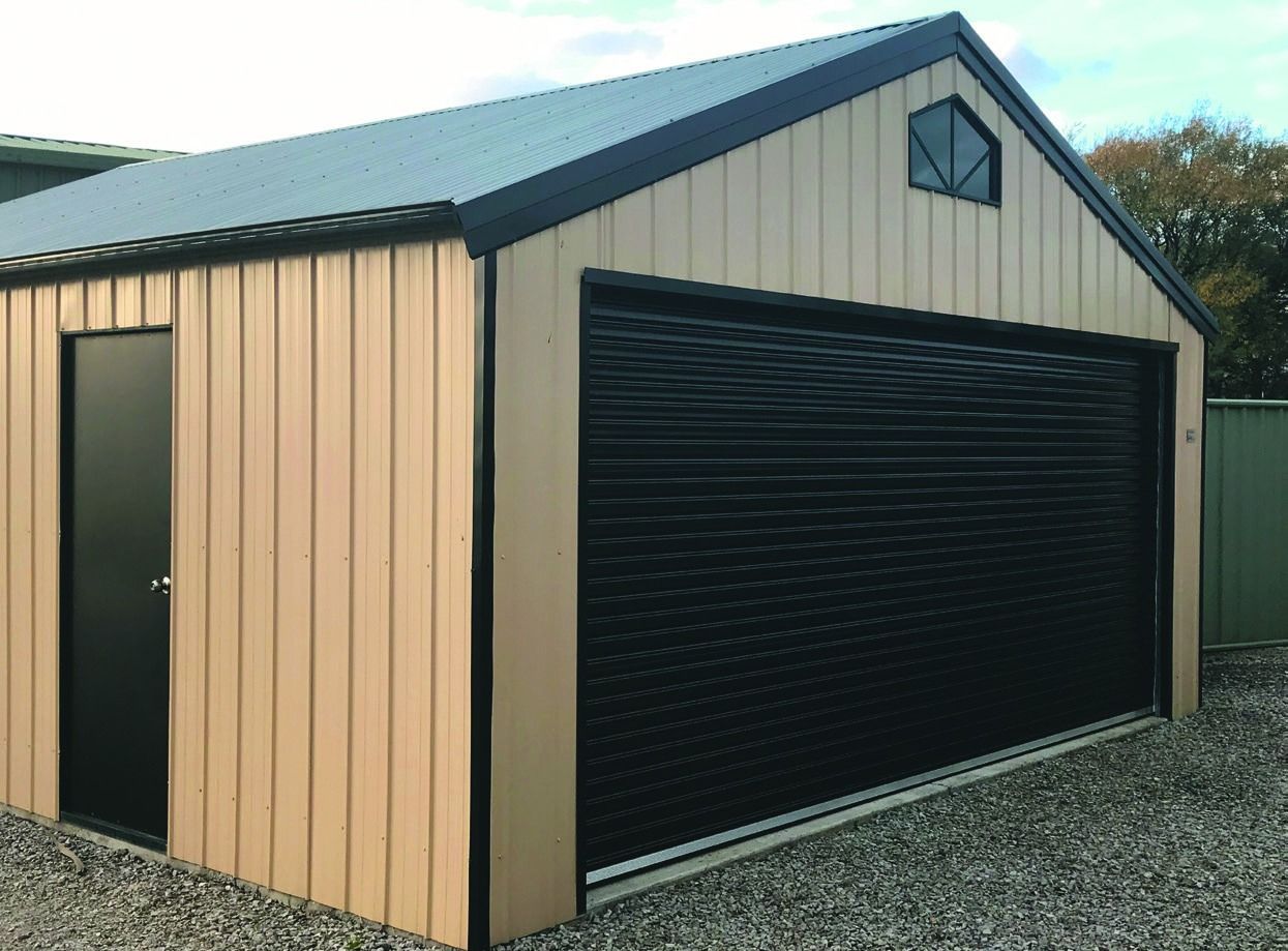 Small beige and green metal shed with a black roll-up garage door on gravel.